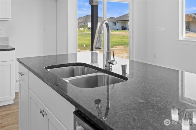 kitchen with light wood-type flooring, dark stone countertops, sink, and white cabinets