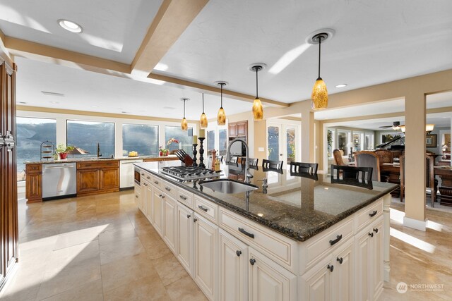 kitchen with dark stone countertops, a center island with sink, hanging light fixtures, appliances with stainless steel finishes, and sink