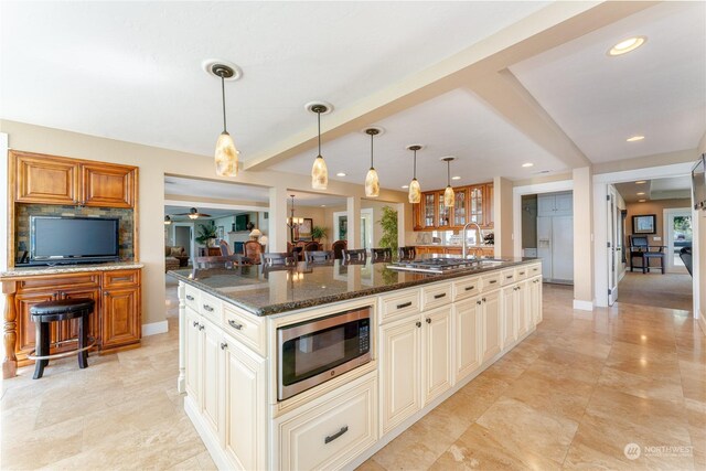 kitchen with dark stone counters, decorative light fixtures, light tile patterned flooring, a large island, and stainless steel microwave