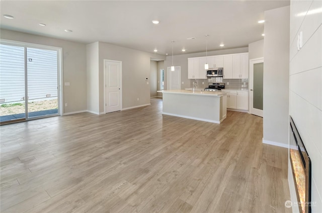 kitchen with appliances with stainless steel finishes, pendant lighting, an island with sink, white cabinets, and light wood-type flooring