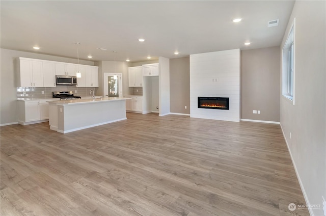 kitchen with white cabinetry, tasteful backsplash, a center island with sink, light wood-type flooring, and appliances with stainless steel finishes