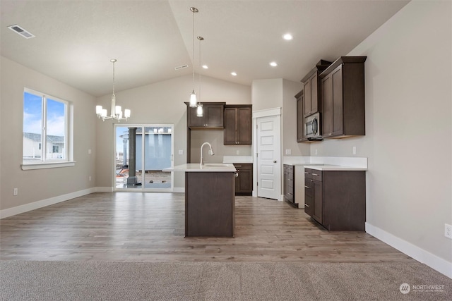 kitchen featuring dark brown cabinetry, sink, hanging light fixtures, vaulted ceiling, and a kitchen island with sink