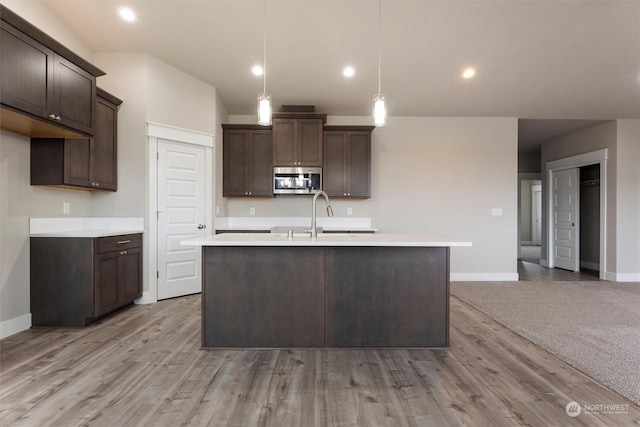 kitchen with dark brown cabinetry, sink, a center island with sink, light hardwood / wood-style floors, and hanging light fixtures