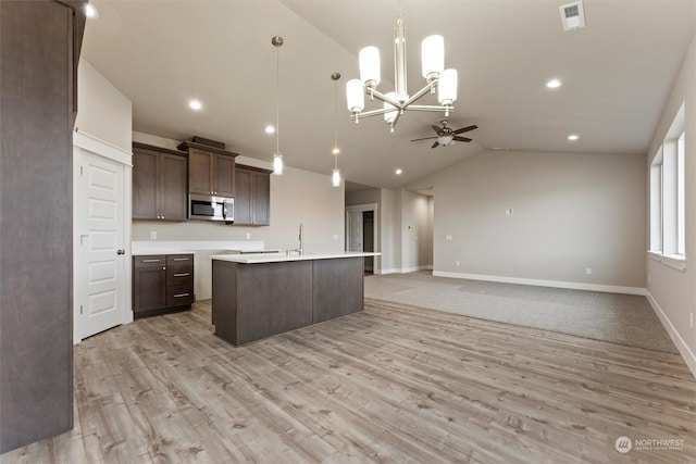 kitchen with a kitchen island with sink, vaulted ceiling, decorative light fixtures, light hardwood / wood-style floors, and dark brown cabinetry