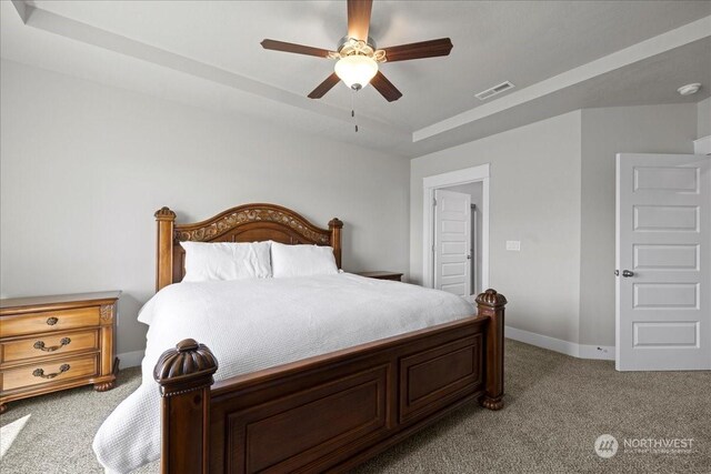 bedroom featuring light colored carpet, a ceiling fan, baseboards, visible vents, and a tray ceiling