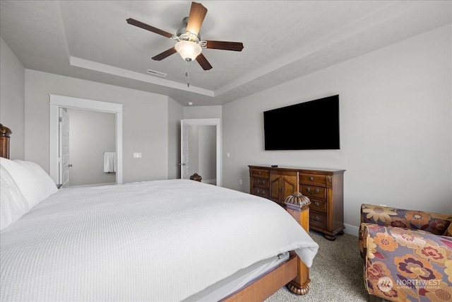 carpeted bedroom featuring a ceiling fan, a tray ceiling, and visible vents