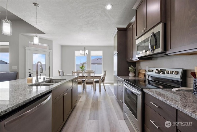 kitchen with dark brown cabinetry, light stone countertops, stainless steel appliances, light wood-style floors, and a sink