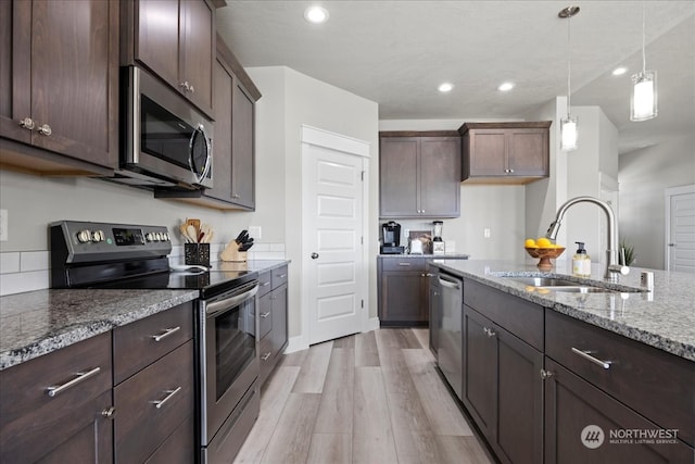 kitchen with dark brown cabinets, sink, light stone countertops, light hardwood / wood-style floors, and appliances with stainless steel finishes