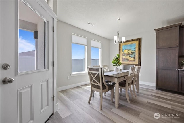 dining space featuring light wood finished floors, baseboards, visible vents, and a notable chandelier