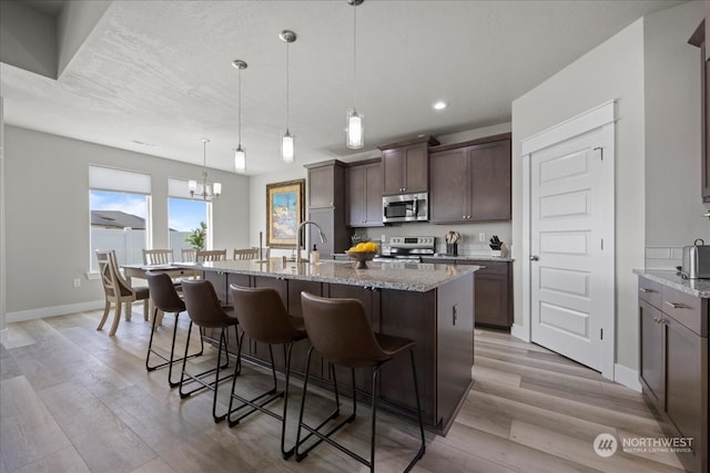 kitchen featuring dark brown cabinets, an inviting chandelier, light hardwood / wood-style floors, light stone countertops, and appliances with stainless steel finishes