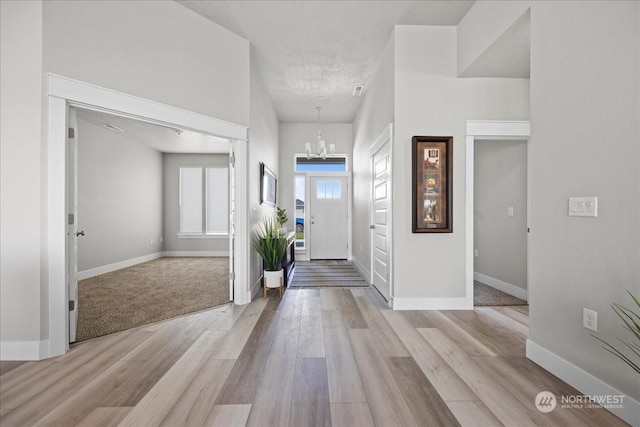 entryway featuring light wood-type flooring, a textured ceiling, baseboards, and an inviting chandelier