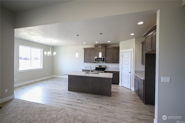 kitchen featuring stainless steel appliances, sink, decorative light fixtures, a kitchen island with sink, and light wood-type flooring