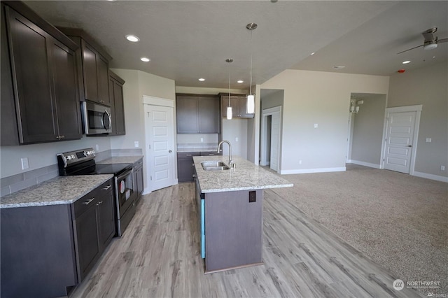 kitchen featuring stainless steel appliances, a kitchen island with sink, a sink, light stone countertops, and baseboards