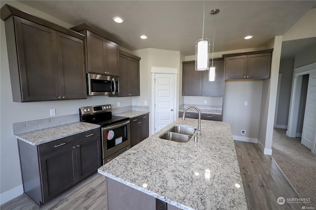 kitchen featuring dark brown cabinetry, light stone counters, stainless steel appliances, light wood-style floors, and a sink