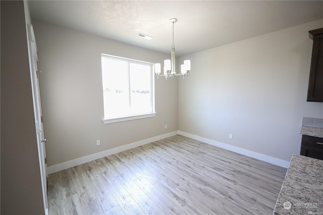 unfurnished dining area with light wood finished floors, an inviting chandelier, visible vents, and baseboards