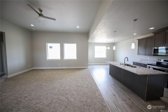 kitchen with stainless steel appliances, a ceiling fan, a kitchen island with sink, a sink, and baseboards