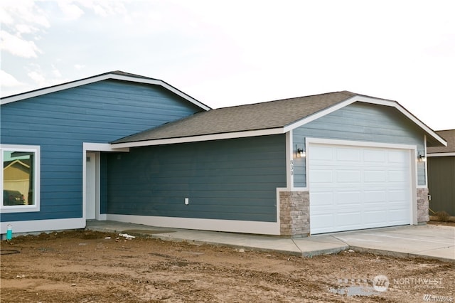 view of side of home with driveway, a shingled roof, and an attached garage