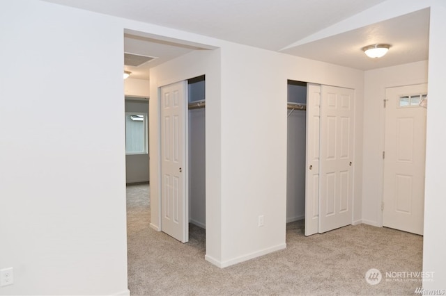 unfurnished bedroom featuring baseboards, carpet flooring, and multiple closets