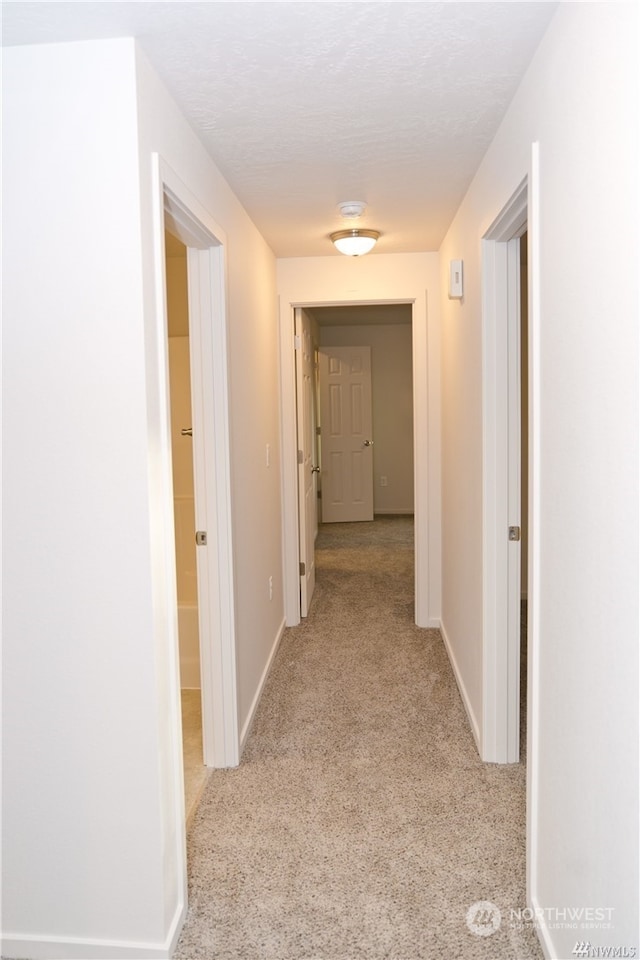 hallway featuring carpet floors, baseboards, and a textured ceiling