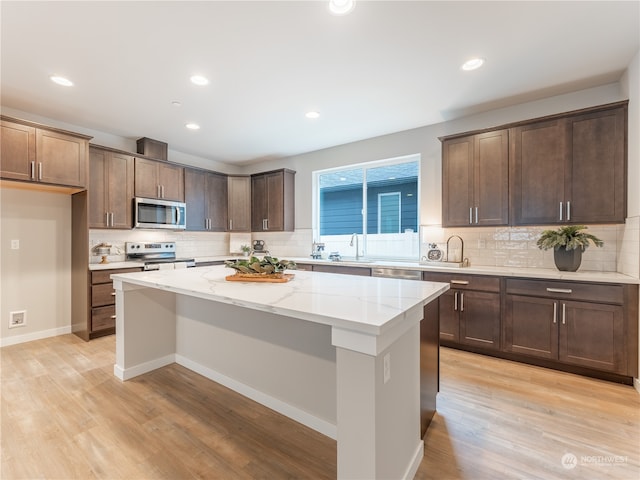 kitchen featuring light stone countertops, appliances with stainless steel finishes, a kitchen island, light hardwood / wood-style floors, and backsplash