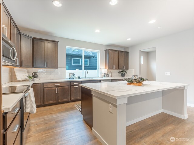 kitchen with a kitchen island, stainless steel appliances, backsplash, light stone counters, and light hardwood / wood-style flooring