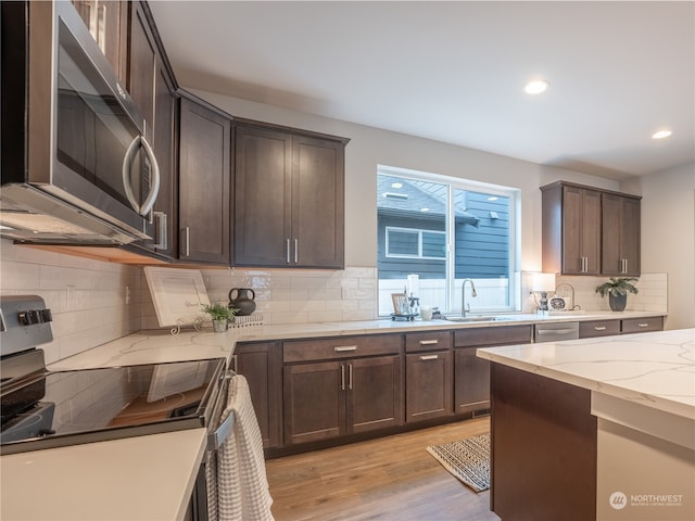 kitchen featuring stainless steel appliances, decorative backsplash, light wood-type flooring, dark brown cabinets, and light stone countertops