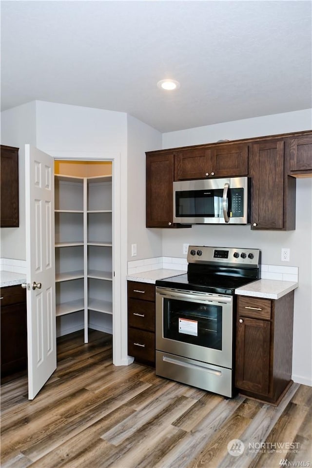 kitchen with recessed lighting, stainless steel appliances, dark brown cabinets, and wood finished floors