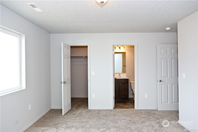 unfurnished bedroom featuring a textured ceiling, carpet flooring, visible vents, a spacious closet, and a closet