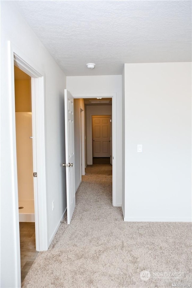 hallway with light colored carpet, a textured ceiling, and baseboards