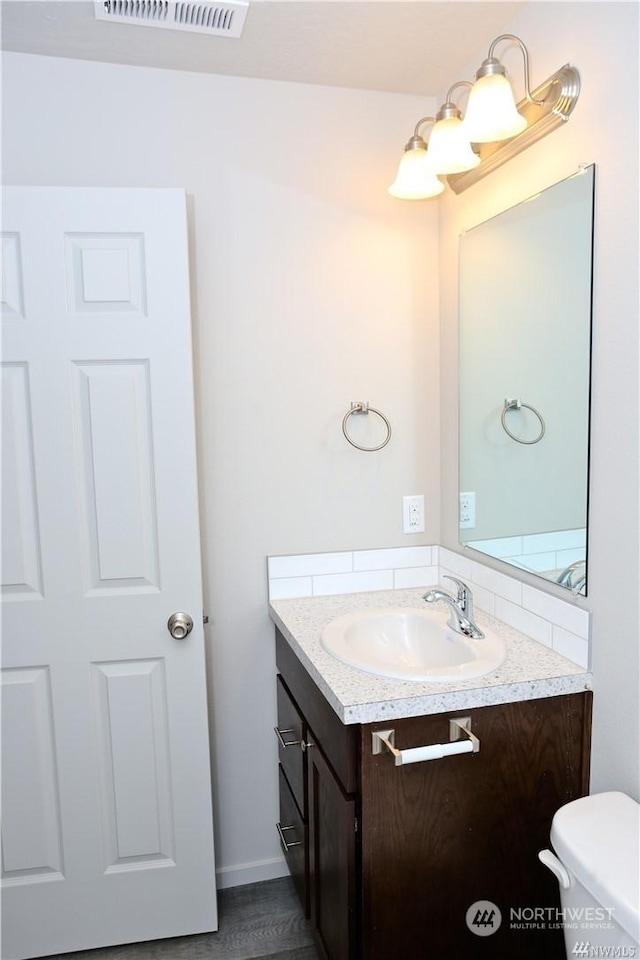 half bathroom featuring visible vents, toilet, and vanity