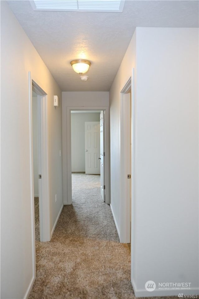 hall with light carpet, a textured ceiling, and baseboards