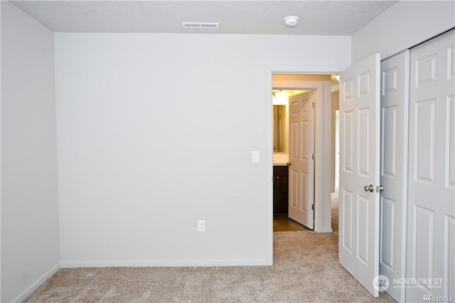 unfurnished bedroom featuring light carpet, baseboards, visible vents, and a closet