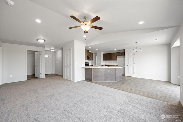 unfurnished living room with lofted ceiling, light colored carpet, recessed lighting, and ceiling fan with notable chandelier