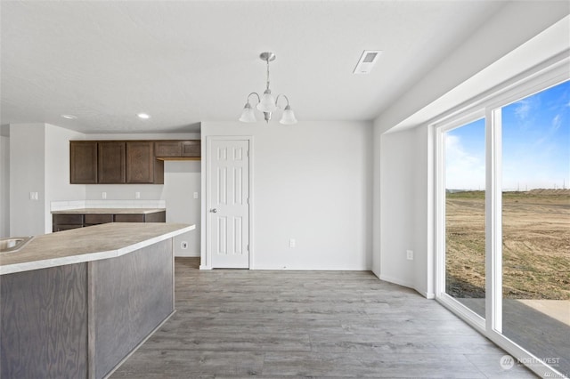 kitchen featuring light countertops, hanging light fixtures, light wood-style flooring, dark brown cabinets, and a chandelier