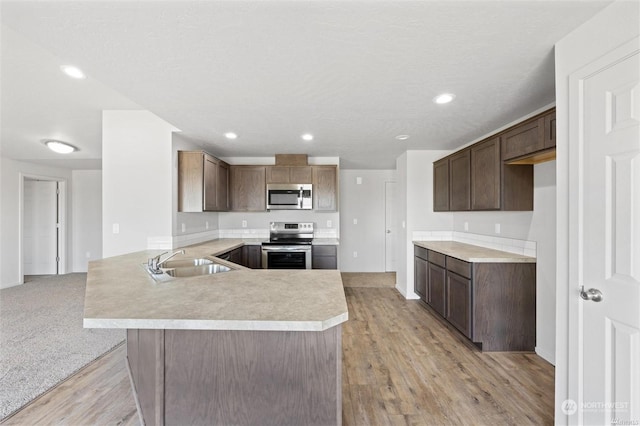 kitchen with light countertops, appliances with stainless steel finishes, light wood-style floors, a sink, and a peninsula