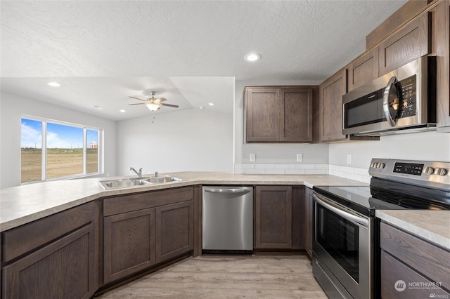 kitchen featuring a ceiling fan, stainless steel appliances, light countertops, light wood-type flooring, and a sink