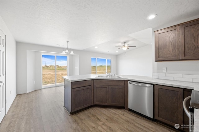 kitchen featuring a peninsula, stainless steel dishwasher, a sink, and light countertops