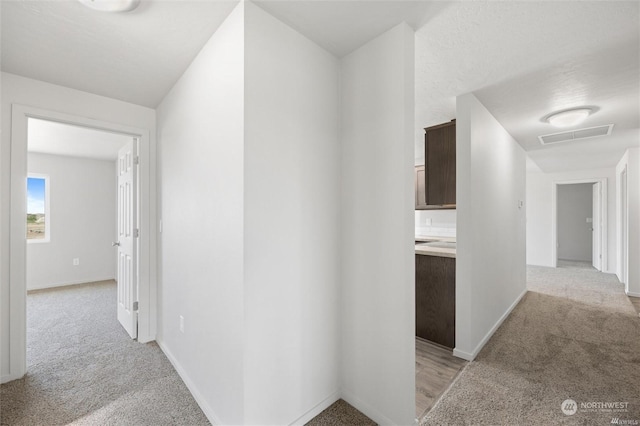 hallway featuring light carpet, visible vents, and baseboards