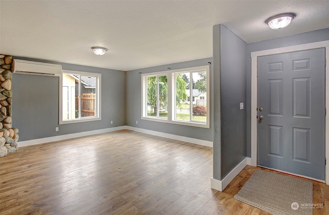 foyer entrance with light hardwood / wood-style floors, an AC wall unit, and a textured ceiling