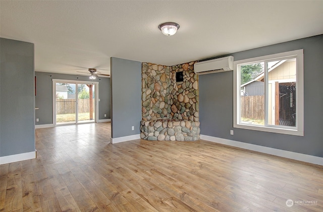 unfurnished living room with ceiling fan, a wall mounted air conditioner, light wood-type flooring, and plenty of natural light