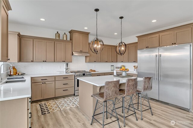 kitchen with decorative light fixtures, a center island, premium appliances, a kitchen breakfast bar, and light hardwood / wood-style floors