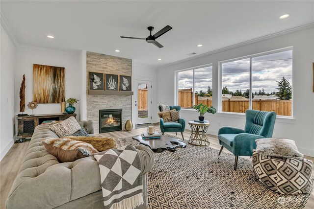 living room with ornamental molding, light hardwood / wood-style floors, a large fireplace, and ceiling fan