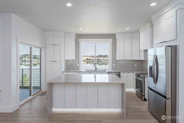 kitchen with stainless steel appliances, white cabinetry, a center island, and light stone counters