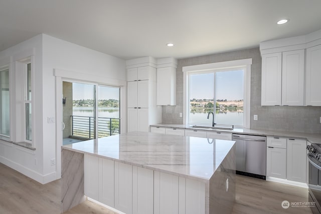 kitchen with sink, appliances with stainless steel finishes, white cabinetry, a center island, and light stone counters