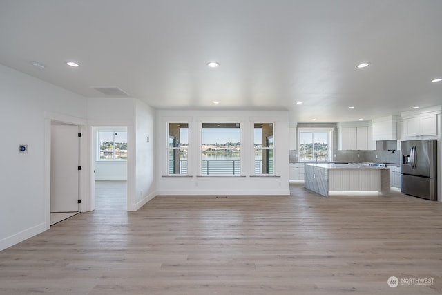 kitchen with white cabinetry, decorative backsplash, a center island, stainless steel refrigerator with ice dispenser, and light hardwood / wood-style flooring