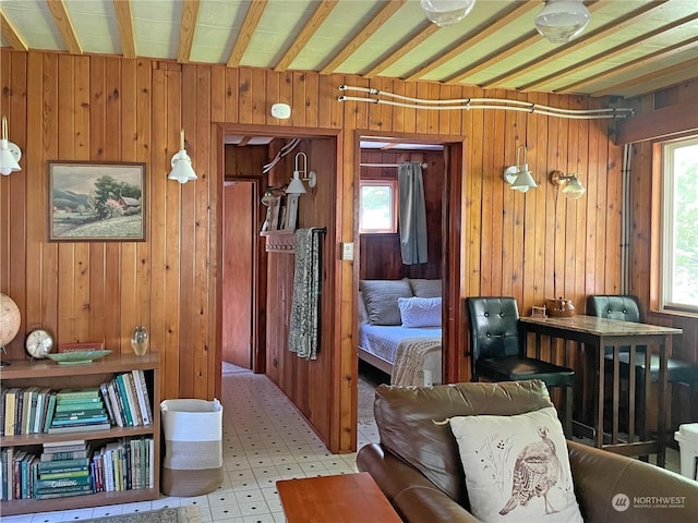 living area with beam ceiling, wooden walls, and light floors