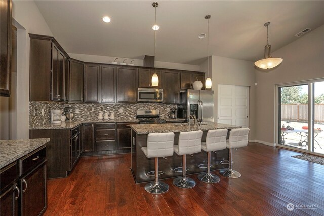 kitchen with dark hardwood / wood-style floors, appliances with stainless steel finishes, decorative backsplash, decorative light fixtures, and a center island with sink