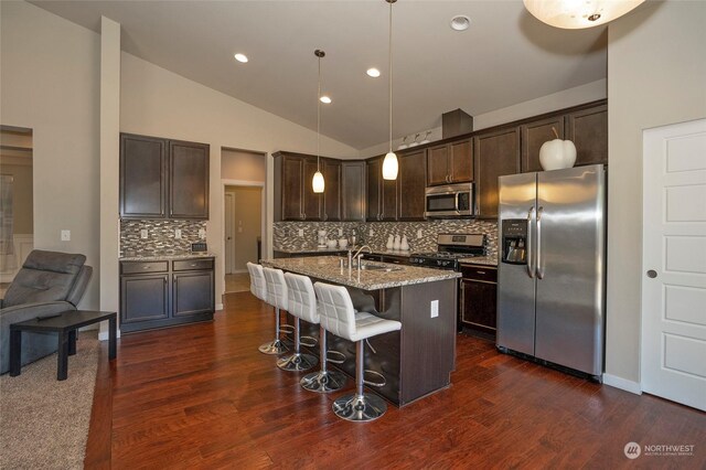 kitchen with dark wood-type flooring, appliances with stainless steel finishes, tasteful backsplash, and a kitchen island with sink