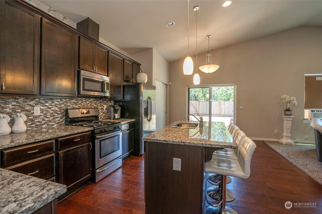 kitchen with dark hardwood / wood-style flooring, a kitchen bar, light stone counters, appliances with stainless steel finishes, and a kitchen island with sink