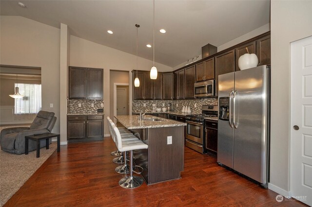 kitchen featuring a kitchen island with sink, lofted ceiling, dark colored carpet, and appliances with stainless steel finishes